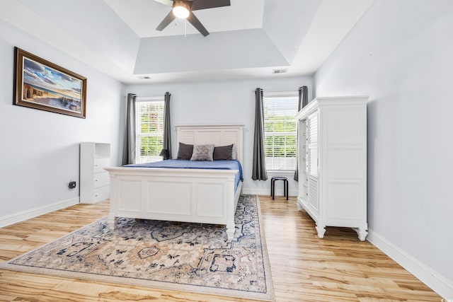 bedroom with a raised ceiling, ceiling fan, and light hardwood / wood-style flooring