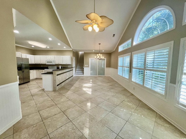 kitchen with stainless steel fridge, high vaulted ceiling, range with electric stovetop, ornamental molding, and white cabinets