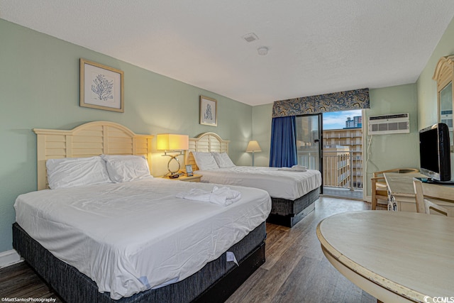 bedroom with a textured ceiling, access to exterior, dark hardwood / wood-style floors, and an AC wall unit