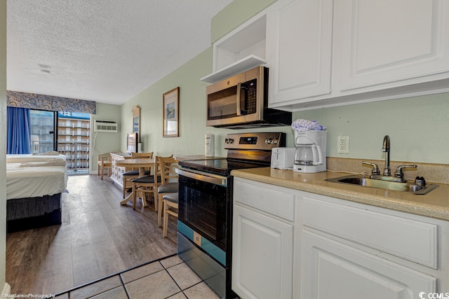 kitchen with a textured ceiling, white cabinets, stainless steel appliances, sink, and light tile patterned floors