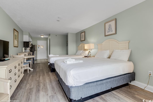 bedroom with stainless steel fridge and light hardwood / wood-style floors