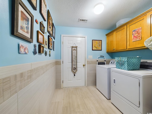 laundry area featuring washing machine and dryer, a textured ceiling, tile walls, and cabinets