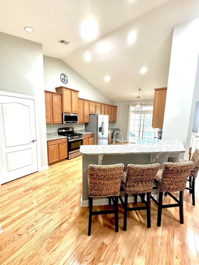 kitchen with light hardwood / wood-style flooring, kitchen peninsula, vaulted ceiling, a breakfast bar area, and appliances with stainless steel finishes