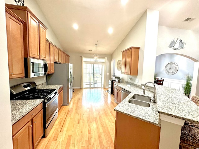 kitchen featuring decorative light fixtures, light stone countertops, light wood-type flooring, appliances with stainless steel finishes, and sink