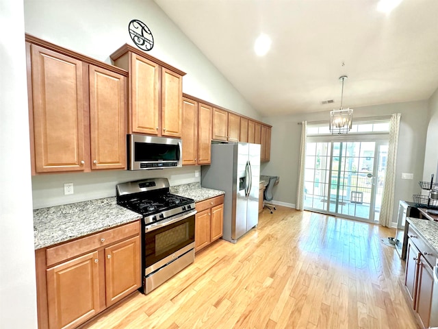 kitchen with a chandelier, light hardwood / wood-style flooring, light stone countertops, appliances with stainless steel finishes, and pendant lighting