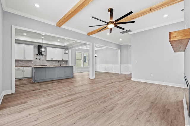 unfurnished living room featuring ceiling fan, ornamental molding, beamed ceiling, and light hardwood / wood-style flooring