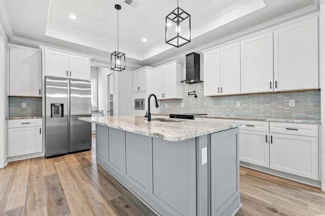 kitchen featuring a raised ceiling, stainless steel built in refrigerator, a center island with sink, sink, and white cabinetry