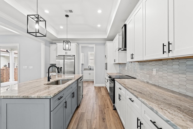 kitchen featuring appliances with stainless steel finishes, an island with sink, sink, white cabinetry, and wall chimney range hood