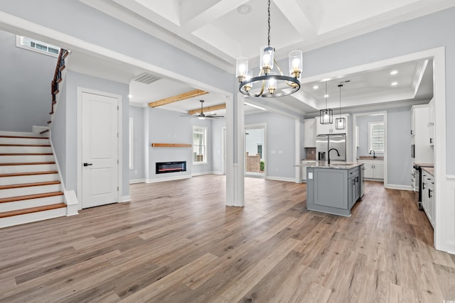 interior space featuring a center island with sink, hanging light fixtures, ceiling fan with notable chandelier, and light wood-type flooring