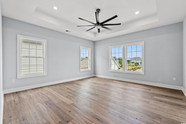 spare room with ceiling fan, wood-type flooring, and a tray ceiling