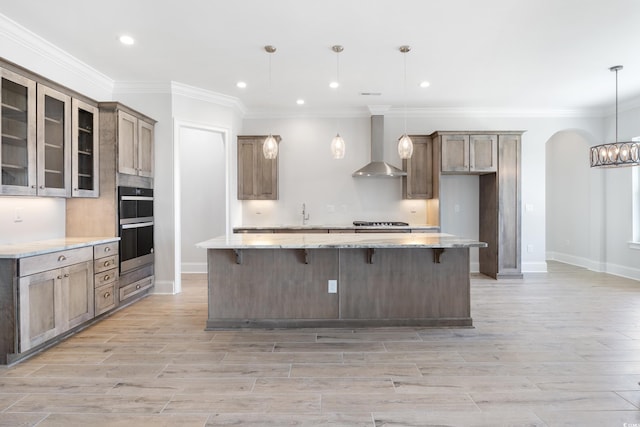 kitchen featuring a spacious island, wall chimney exhaust hood, a kitchen bar, light wood-type flooring, and pendant lighting