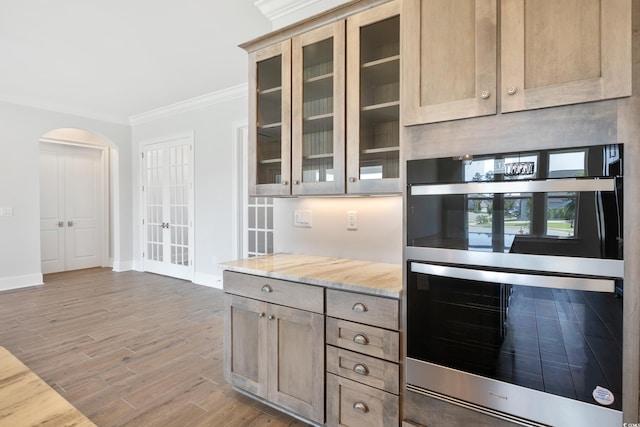 kitchen with wood-type flooring, stainless steel double oven, crown molding, light stone countertops, and light brown cabinets