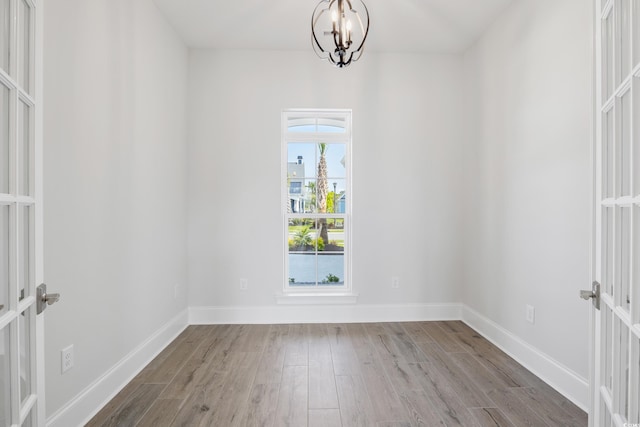 empty room with an inviting chandelier, light hardwood / wood-style floors, and french doors