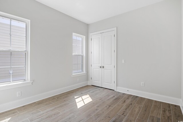 unfurnished bedroom with multiple windows, light hardwood / wood-style floors, and a closet