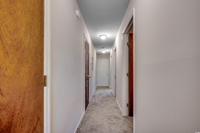 hallway with a textured ceiling and light carpet