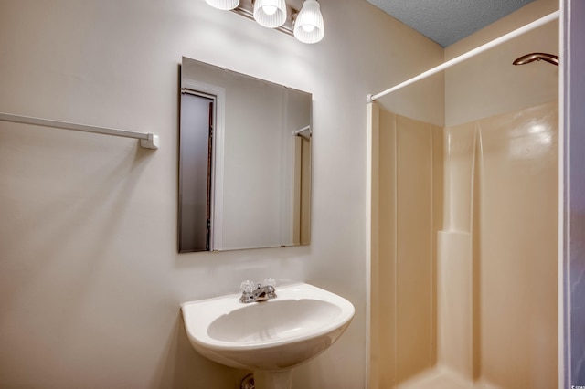 bathroom with a textured ceiling, a shower, and sink