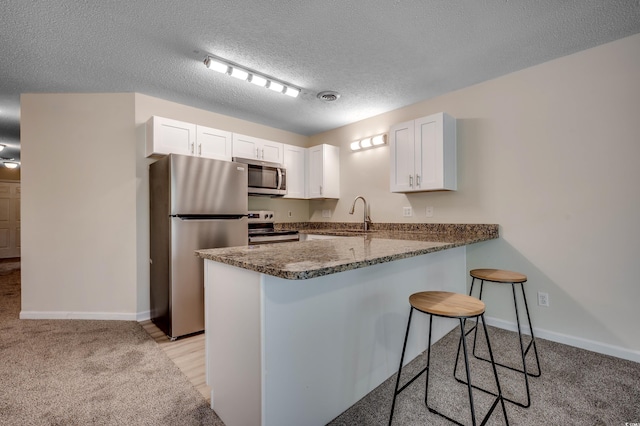 kitchen with dark stone counters, a kitchen breakfast bar, kitchen peninsula, appliances with stainless steel finishes, and white cabinets