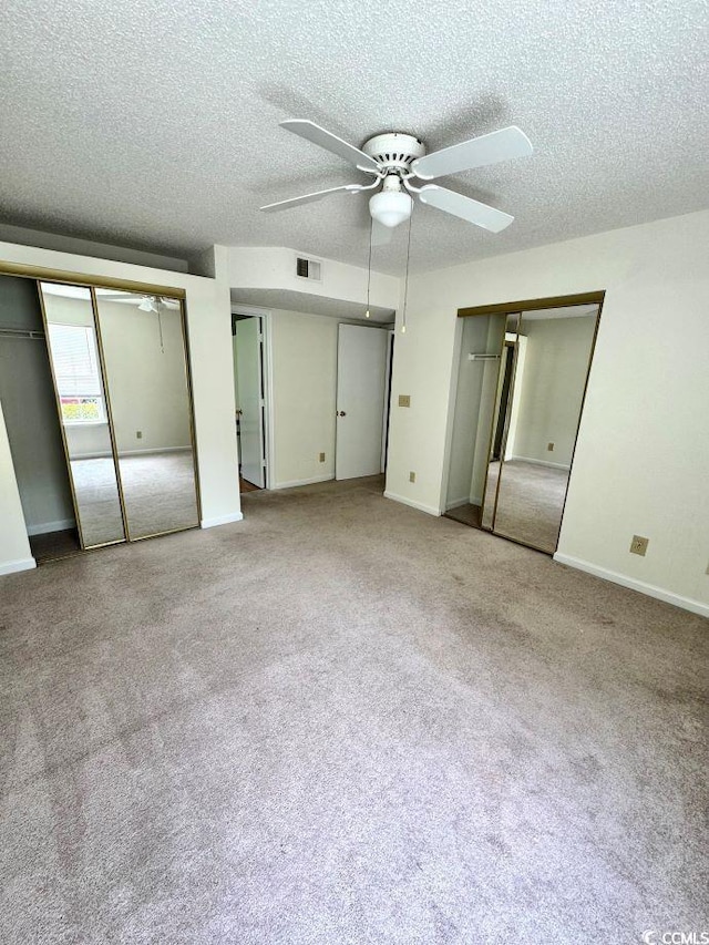 unfurnished bedroom with a textured ceiling, light colored carpet, ceiling fan, and multiple closets