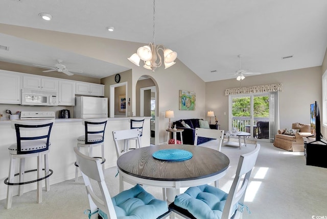 dining space with ceiling fan with notable chandelier, light colored carpet, and vaulted ceiling