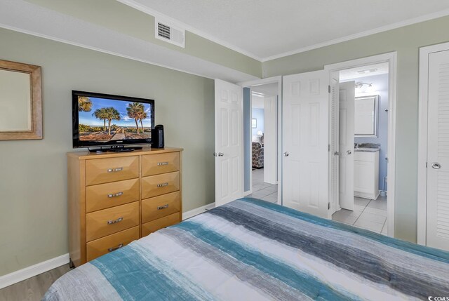 bedroom featuring ensuite bathroom, ornamental molding, and light tile flooring