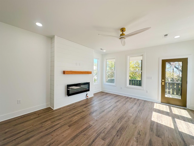 unfurnished living room with a ceiling fan, visible vents, a large fireplace, wood finished floors, and baseboards