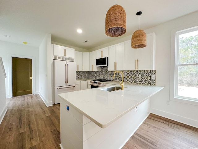 kitchen featuring premium appliances, a sink, white cabinets, light countertops, and pendant lighting