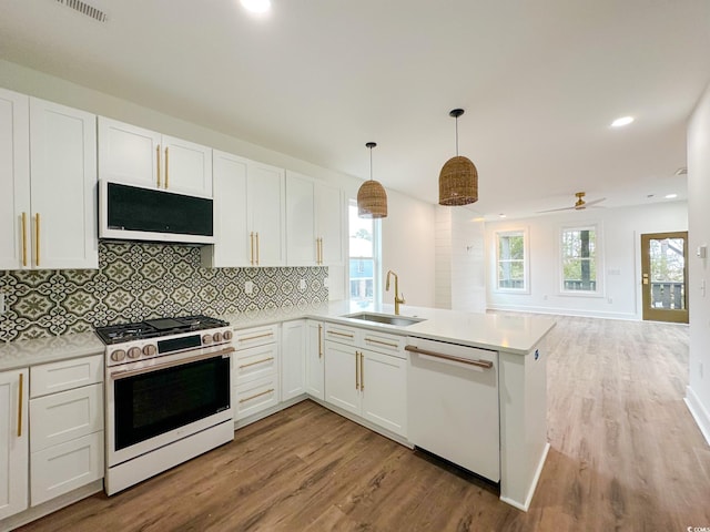 kitchen with a peninsula, white appliances, a sink, white cabinetry, and hanging light fixtures