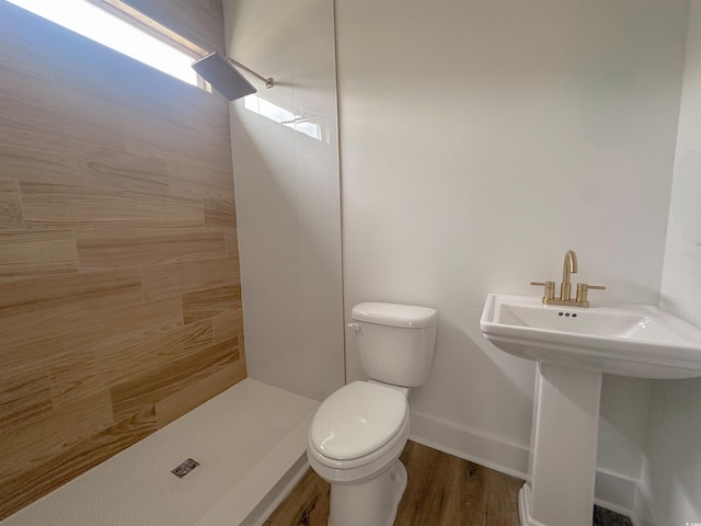 full bathroom with toilet, baseboards, tiled shower, and wood finished floors