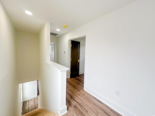 hallway with baseboards, visible vents, wood finished floors, an upstairs landing, and recessed lighting