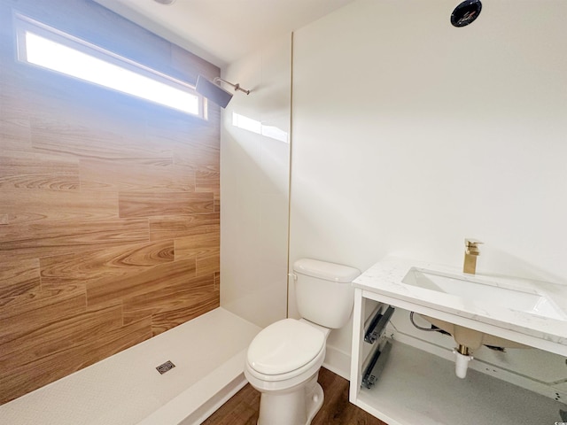 bathroom featuring toilet, tiled shower, and wood finished floors