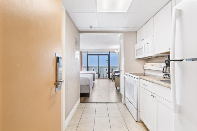 kitchen featuring a drop ceiling, white appliances, white cabinets, light tile patterned flooring, and a wall of windows