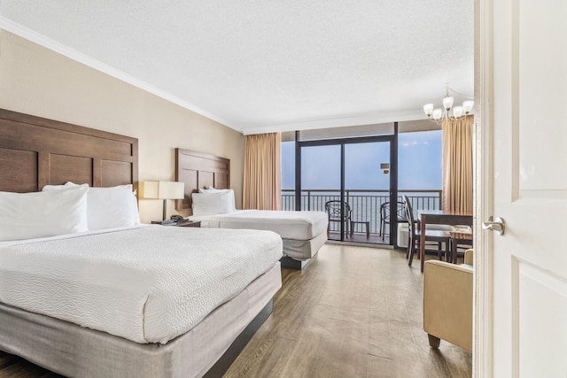 bedroom with access to exterior, a textured ceiling, wood-type flooring, a wall of windows, and a chandelier