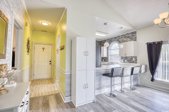 kitchen with white cabinets, decorative light fixtures, a textured ceiling, and a breakfast bar