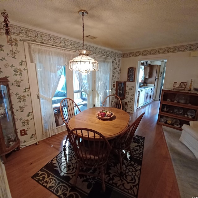 dining area featuring hardwood / wood-style floors, a notable chandelier, ornamental molding, and a textured ceiling