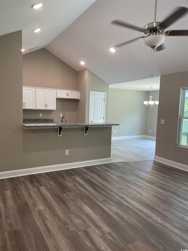 kitchen featuring a breakfast bar, ceiling fan with notable chandelier, vaulted ceiling, dark hardwood / wood-style flooring, and white cabinetry