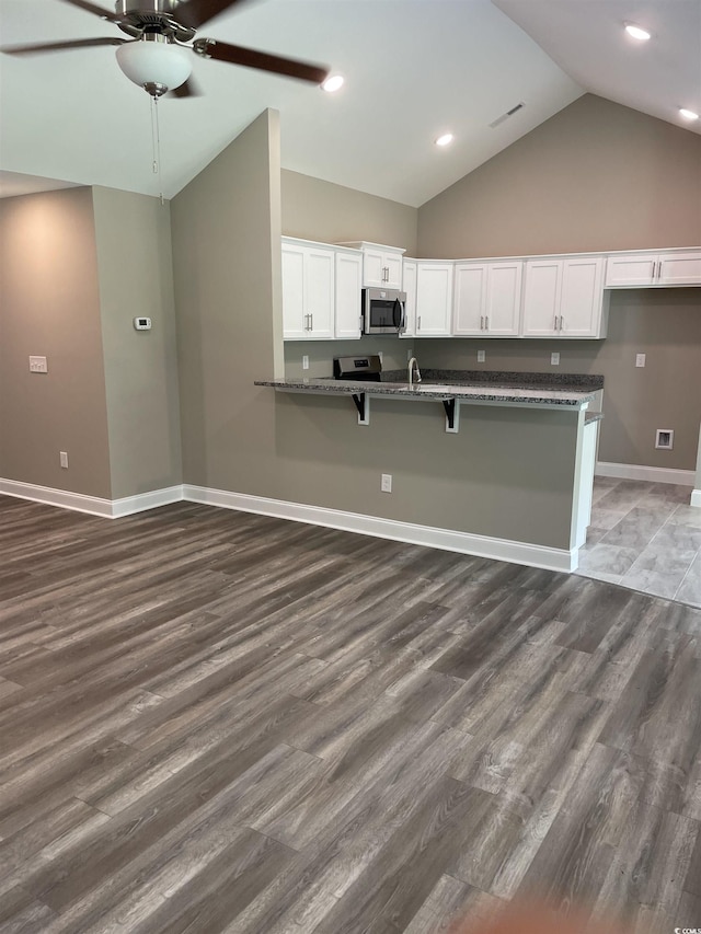 kitchen with dark wood-type flooring, white cabinets, ceiling fan, dark stone countertops, and a kitchen bar