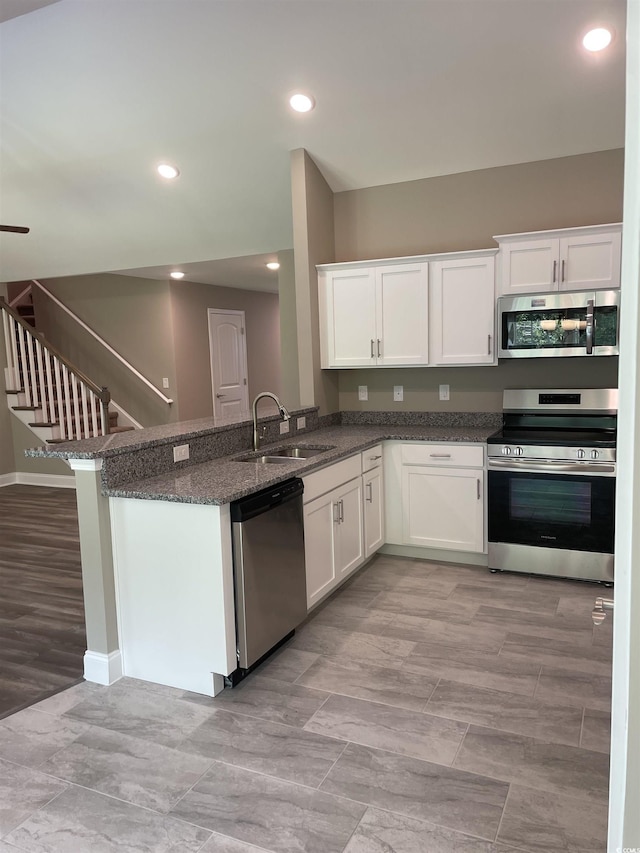 kitchen with kitchen peninsula, appliances with stainless steel finishes, dark stone counters, sink, and white cabinetry