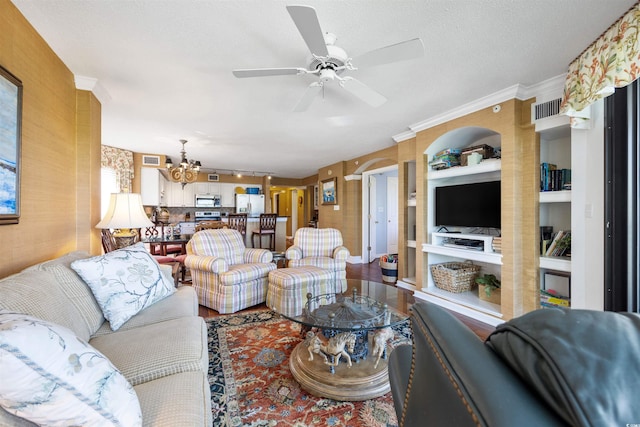 living room with a textured ceiling, ornamental molding, ceiling fan with notable chandelier, built in shelves, and wood-type flooring