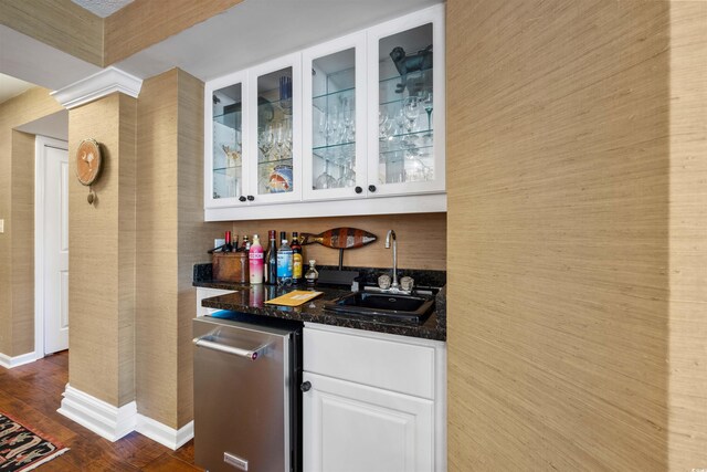 bar featuring white cabinetry, stainless steel dishwasher, dark wood-type flooring, dark stone countertops, and sink