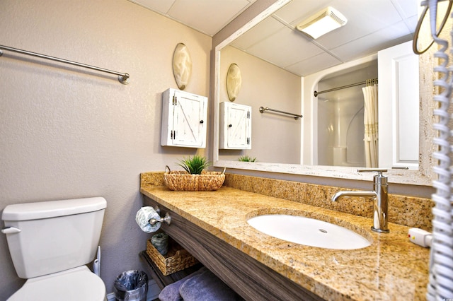 bathroom with toilet, a shower with curtain, a drop ceiling, and vanity