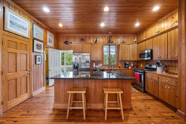 kitchen with a kitchen island, wood walls, appliances with stainless steel finishes, light hardwood / wood-style flooring, and wood ceiling