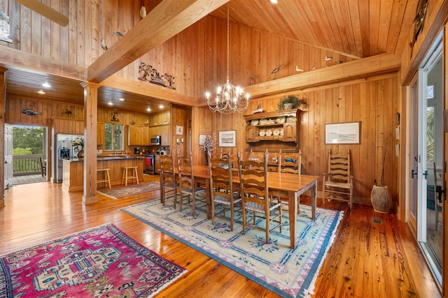 dining space with an inviting chandelier, wooden walls, wood-type flooring, and a towering ceiling