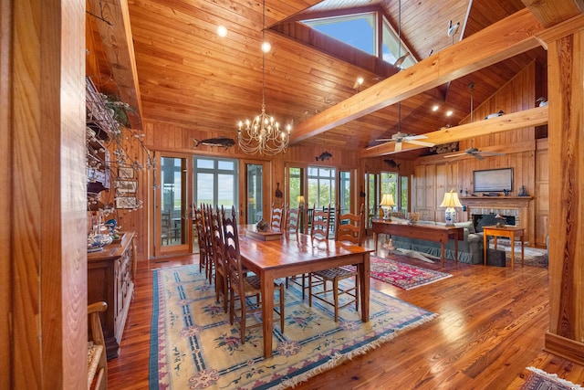 dining room with wooden walls, ceiling fan with notable chandelier, hardwood / wood-style floors, and beam ceiling