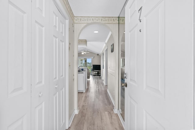 hallway with light wood-type flooring and vaulted ceiling