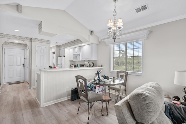 dining space with a notable chandelier, vaulted ceiling, and light wood-type flooring