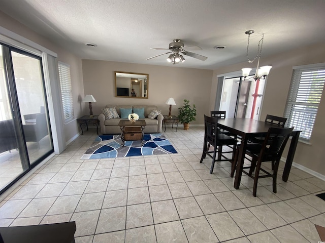 dining space with a textured ceiling, light tile patterned flooring, and ceiling fan with notable chandelier