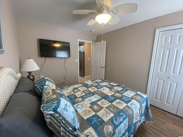 bedroom with stainless steel refrigerator, ceiling fan, a closet, and hardwood / wood-style floors