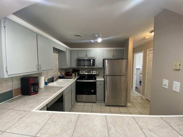 kitchen with tile counters, sink, stainless steel appliances, and tasteful backsplash