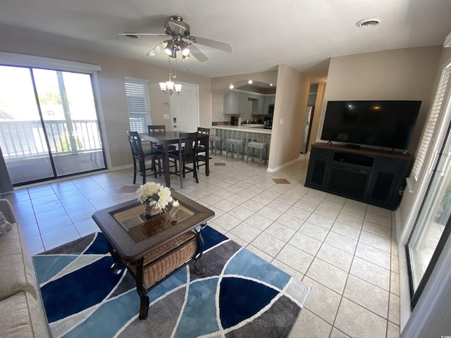 tiled living room with ceiling fan with notable chandelier