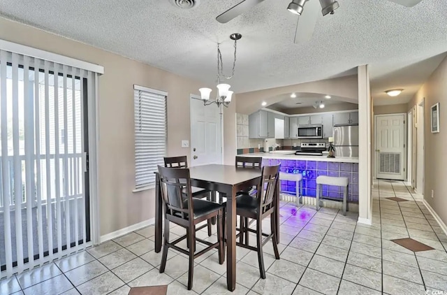 dining space with a textured ceiling, light tile patterned floors, and ceiling fan with notable chandelier